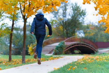 Bir kız yol boyunca yürür ve sonbaharın tadını çıkarır. Sarı yapraklı akçaağaçlar ve nehir üzerinde bir köprü.