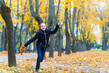 Parkta koşan ve sonbaharın tadını çıkaran bir kız, sarı yapraklı güzel bir doğa.