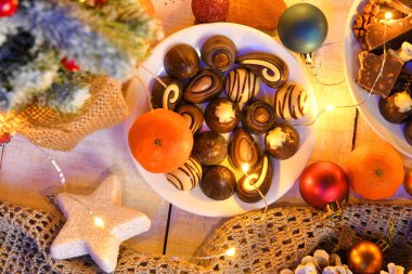 Mutlu noeller ya da gece aydınlatma ile yeni yıl dekorasyonu için tatlı yemek üst görünümü - çikolata şekerler, mandalinalar, beyaz ahşap üzerinde kurabiyeler