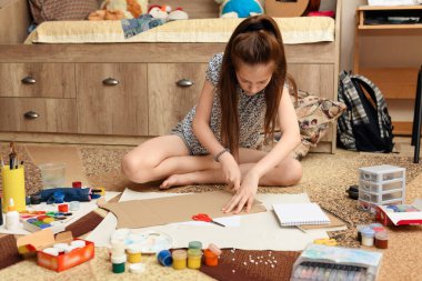 Kız evde resim çiziyor, sanat eseri yapıyor, kağıt, boya ve fırçalardan yaratıcı sanat eserleri yapıyor.