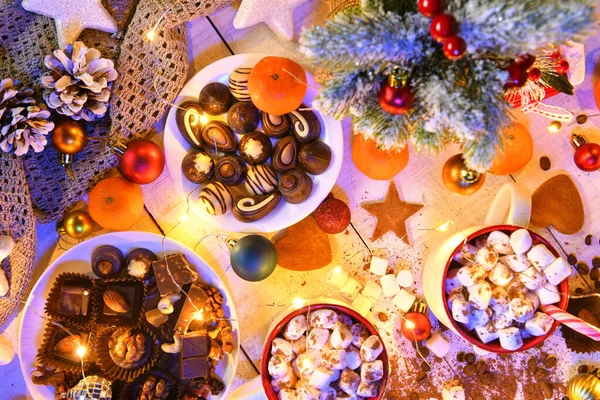 甘い食べ物のトップビューの背景メリークリスマスや夜のイルミネーションで新年の休日の装飾 白い木のチョコレートキャンディー みかん クッキー マシュマロ ココアラテ — ストック写真