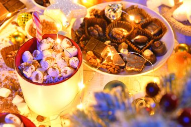 Mutlu noeller ya da gece aydınlatmalı yeni yıl dekorasyonu için tatlı yemek üst görünümü - çikolata şekerlemeleri, mandalinalar, kurabiyeler, marşmelov ve beyaz ahşap üzerine kakao latte