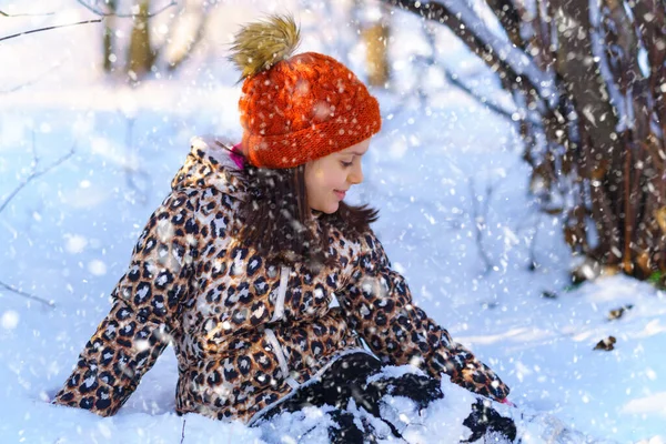 Çocuk oturuyor ve kış ormanlarında eğleniyor. Parlak güneş ışığı ve kardaki gölgeler, güzel doğa..