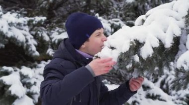 Genç bir çocuk kış ormanında kar yiyor, parlak karlı köknar ağaçları, güzel doğa.