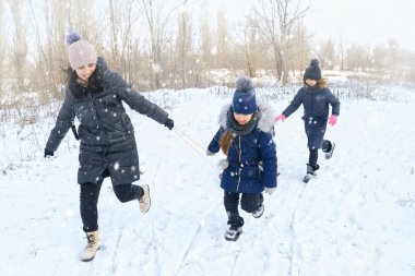 Kışın açık havada aile oyunları ve kızak gezintileri, anne ve çocuklar karlı kışta eğleniyorlar.