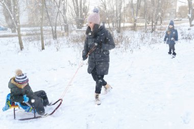 Kışın açık havada aile oyunları ve kızak gezintileri, anne ve çocuklar karlı kışta eğleniyorlar.
