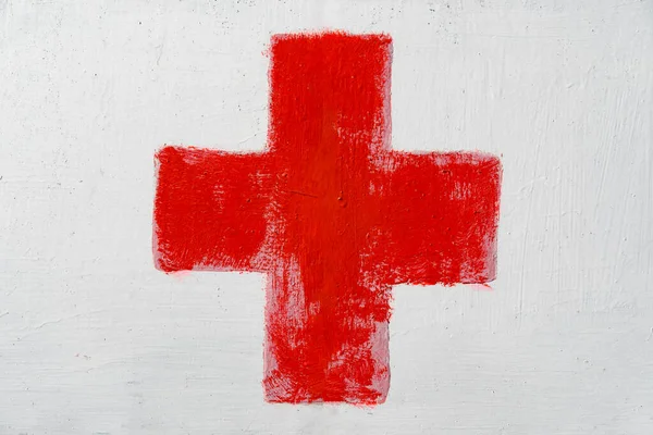 Red cross painted by hand on white wall. First aid kit medical icon. Medicine health hospital sign or emergency medicine symbol, health care.