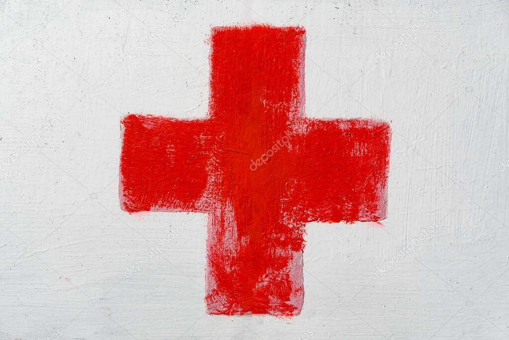Red cross painted by hand on white wall. First aid kit medical icon. Medicine health hospital sign or emergency medicine symbol, health care.