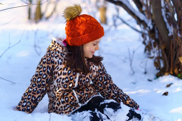 Çocuk oturuyor ve kış ormanlarında eğleniyor. Parlak güneş ışığı ve kardaki gölgeler, güzel doğa..