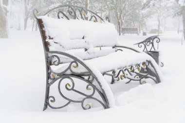 Kış şehri parkı, kar ve karla kaplı banklar.