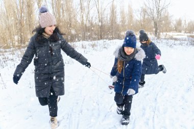Kışın açık havada aile oyunları ve kızak gezintileri, anne ve çocuklar karlı kışta eğleniyorlar.