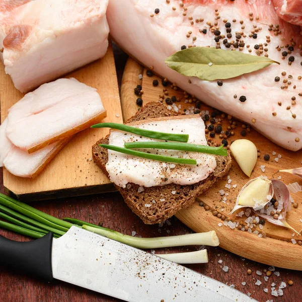 Kesme tahtasında tuzlu, baharatlı ve sarımsaklı çiğ domuz eti ve domuz yağı, koyu ahşap arka plan