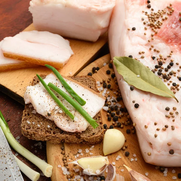 Kesme tahtasında tuzlu, baharatlı ve sarımsaklı çiğ domuz eti ve domuz yağı, koyu ahşap arka plan