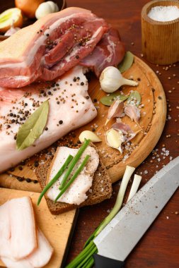 Kesme tahtasında tuzlu, baharatlı ve sarımsaklı çiğ domuz eti ve domuz yağı, koyu ahşap arka plan