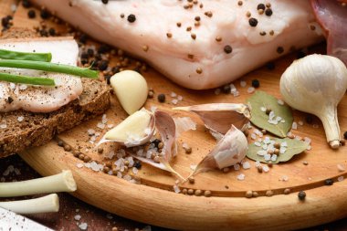 Kesme tahtasında tuzlu, baharatlı ve sarımsaklı çiğ domuz eti ve domuz yağı, koyu ahşap arka plan