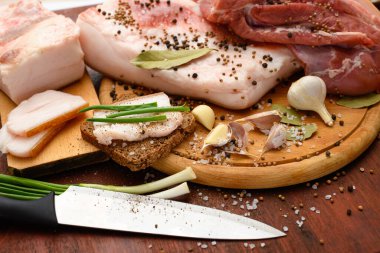 Kesme tahtasında tuzlu, baharatlı ve sarımsaklı çiğ domuz eti ve domuz yağı, koyu ahşap arka plan