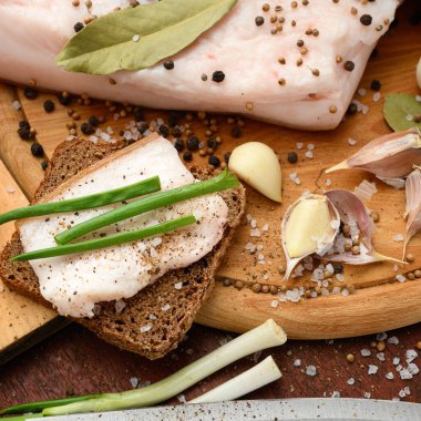 Kesme tahtasında tuzlu, baharatlı ve sarımsaklı çiğ domuz eti ve domuz yağı, koyu ahşap arka plan