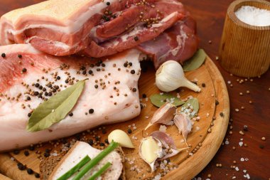 Kesme tahtasında tuzlu, baharatlı ve sarımsaklı çiğ domuz eti ve domuz yağı, koyu ahşap arka plan