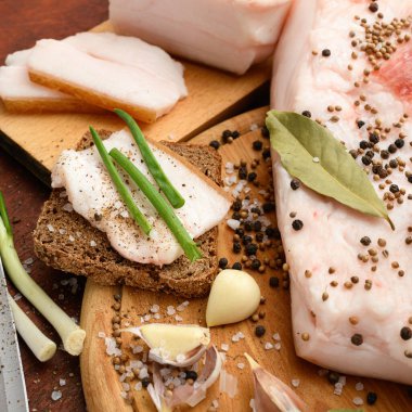 Kesme tahtasında tuzlu, baharatlı ve sarımsaklı çiğ domuz eti ve domuz yağı, koyu ahşap arka plan