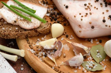 Kesme tahtasında tuzlu, baharatlı ve sarımsaklı çiğ domuz eti ve domuz yağı, koyu ahşap arka plan