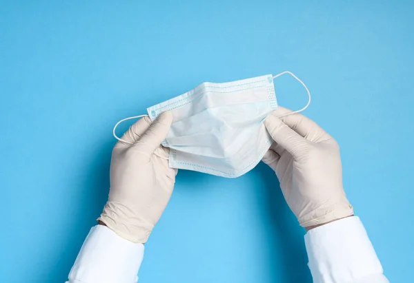 hands in medical gloves with a medical breathing mask on a blue background, health care prevention of coronavirus infection, as well as other viruses and pollution