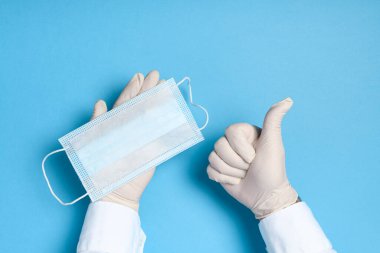 Mavi arka planda tıbbi maske takan elleri tıbbi eldivenlerde, Coronavirus enfeksiyonunun yanı sıra diğer virüsleri ve kirliliği önleyen sağlık hizmetleri