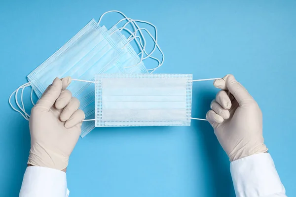 hands in medical gloves with a medical breathing mask on a blue background, health care prevention of coronavirus infection, as well as other viruses and pollution