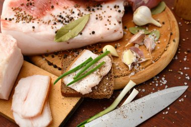 Kesme tahtasında tuzlu, baharatlı ve sarımsaklı çiğ domuz eti ve domuz yağı, koyu ahşap arka plan