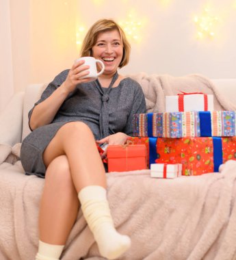 Bir kadının portresi, kanepede oturur ve çay içer, duvarda tatil ışıkları.