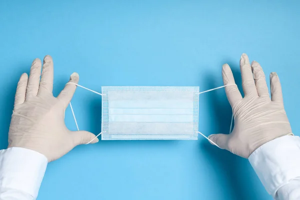 hands in medical gloves with a medical breathing mask on a blue background, health care prevention of coronavirus infection, as well as other viruses and pollution