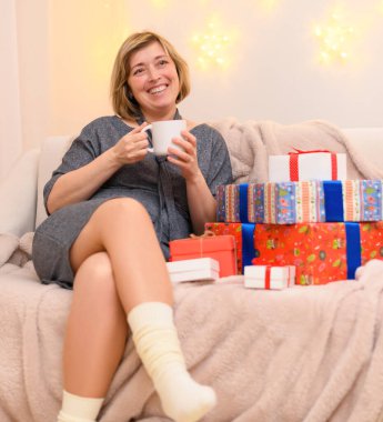 Bir kadının portresi, kanepede oturur ve çay içer, duvarda tatil ışıkları.