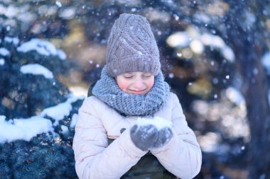 Genç kız kış ormanında poz veriyor, bir avuç karı var ve oynuyor.