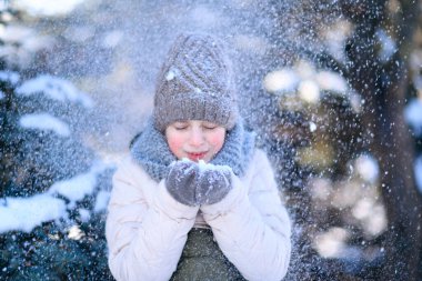 Genç bir kız kış ormanında poz verir, bir avuç karı vardır ve karın üzerine üfler.