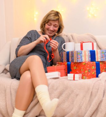 Bir kadının portresi, kanepeye oturur ve hediyeleri açar, duvarda tatil ışıkları.