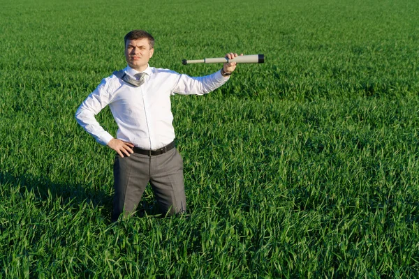 businessman poses with a spyglass, he looks into the distance and looks for something, green grass and blue sky as background