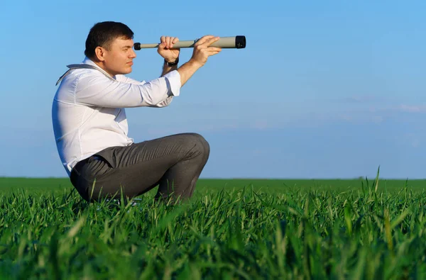 商人在绿地里摆着一副望远镜的样子 他看上去像是个想法或什么的 商业概念 绿草和蓝天作为背景 — 图库照片