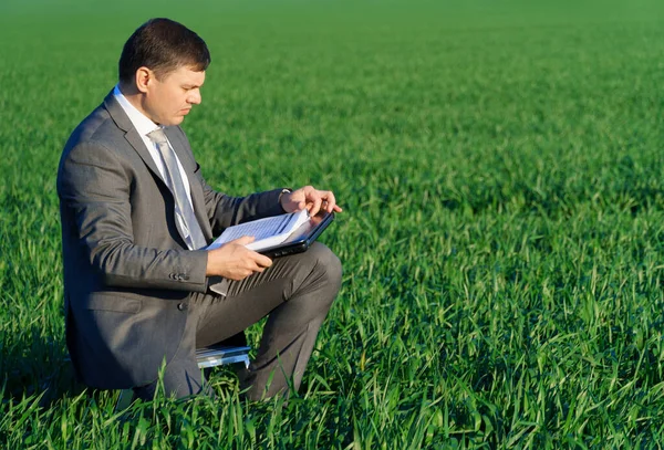 stock image businessman works in a green field, freelance and business concept, green grass and blue sky as background