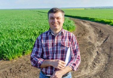 Çiftçi kılığında bir adam, ekose gömlek ve kot giymiş bir şekilde tarlada poz verir, genç lahanaları, buğday, arpa, çavdar veya diğer mısır gevreklerini, tarım ve tarım kavramını kontrol eder ve inceler.