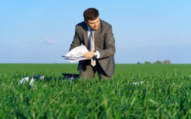 İş adamı yeşil bir alanda çalışır, serbest ve iş kavramı, arka plan olarak yeşil çimenler ve mavi gökyüzü