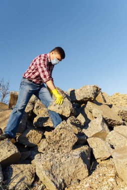 Bir adam taş yığını ve kırık beton parçalarıyla çalışır, inşaat enkazı taşır.