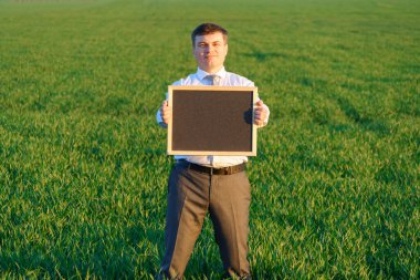 İş adamı elinde boş bir karatahta tutuyor ve yeşil bir çimenlik alanda poz veriyor - iş konsepti