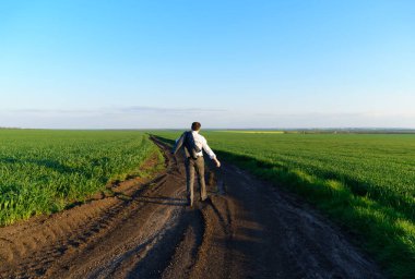İş adamı bir kır yolu boyunca yürüyor, yeşil alan, serbest ve iş konsepti, arka plan olarak yeşil çimen ve mavi gökyüzü
