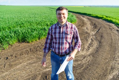 Çiftçi kılığında bir adam, ekose gömlek ve kot giymiş bir şekilde tarlada poz verir, genç lahanaları, buğday, arpa, çavdar veya diğer mısır gevreklerini, tarım ve tarım kavramını kontrol eder ve inceler.