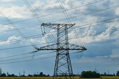 Mavi gökyüzüne karşı yüksek voltajlı elektrik hatları, kuleler ve endüstriyel altyapı