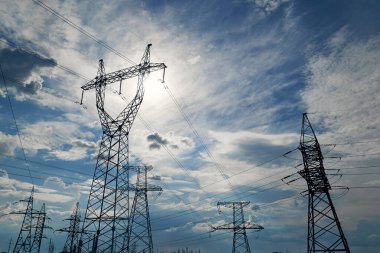 Mavi gökyüzüne karşı yüksek voltajlı elektrik hatları, kuleler ve endüstriyel altyapı