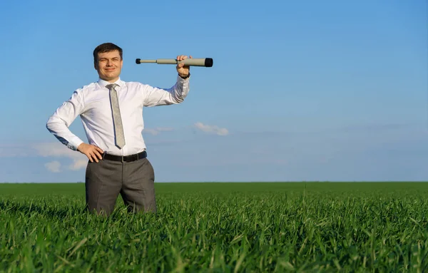 businessman poses with a spyglass, he looks into the distance and looks for something, green grass and blue sky as background