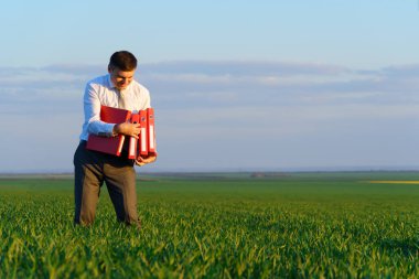 İş adamının elinde yeşil çimenlik alanda dokümanları olan kırmızı bir ofis dosyası var - iş konsepti