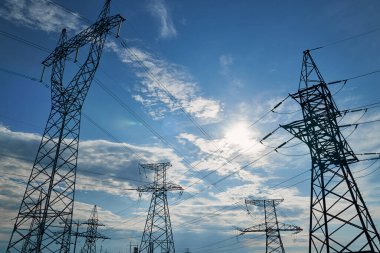 Mavi gökyüzüne karşı yüksek voltajlı elektrik hatları, kuleler ve endüstriyel altyapı