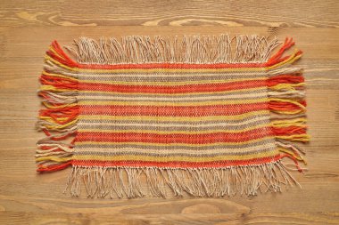 Kırmızı ve sarı yün ipliklerden örülmüş küçük bir el yapımı halı ya da hasırdır. Ahşap arka planda yakın plan bir nesne.