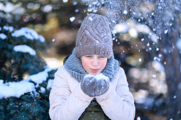 a teenage girl poses in a winter forest, she has a handful of snow and she blows on the snow